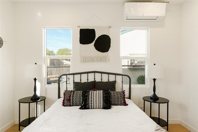 bedroom with baseboards, wood finished floors, and a wall mounted AC