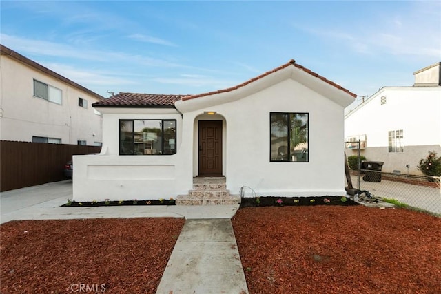 mediterranean / spanish house featuring stucco siding, a tile roof, and fence