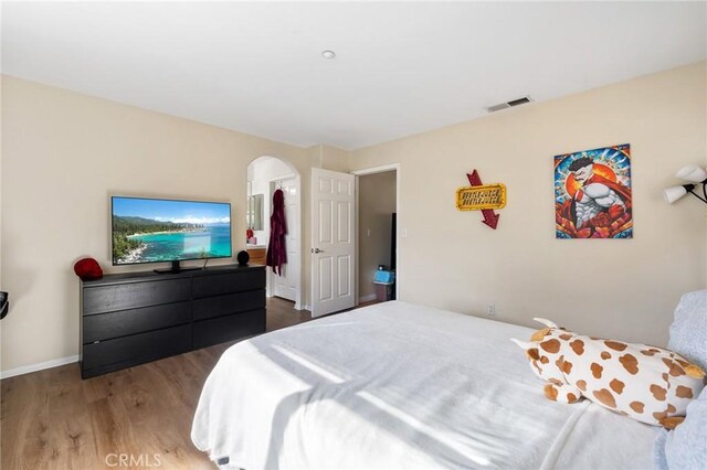 bedroom with arched walkways, wood finished floors, visible vents, and baseboards
