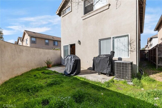 back of house featuring a lawn, central AC, a fenced backyard, and stucco siding