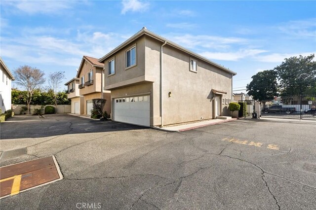 view of property exterior with stucco siding, a gate, fence, and uncovered parking