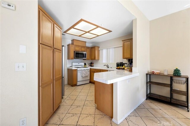 kitchen featuring a peninsula, a sink, stainless steel microwave, white gas stove, and tile counters