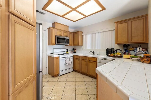 kitchen with stainless steel appliances, a sink, visible vents, tile countertops, and light tile patterned floors