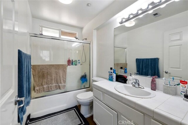 full bath with toilet, vanity, visible vents, and combined bath / shower with glass door