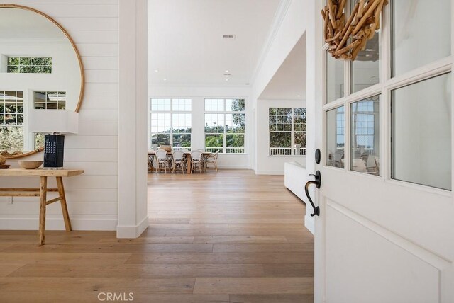 hall featuring baseboards, wood finished floors, visible vents, and ornamental molding