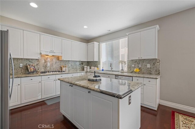 kitchen with a center island, under cabinet range hood, decorative backsplash, stainless steel appliances, and a sink