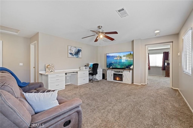 living area with visible vents, baseboards, a ceiling fan, and light carpet