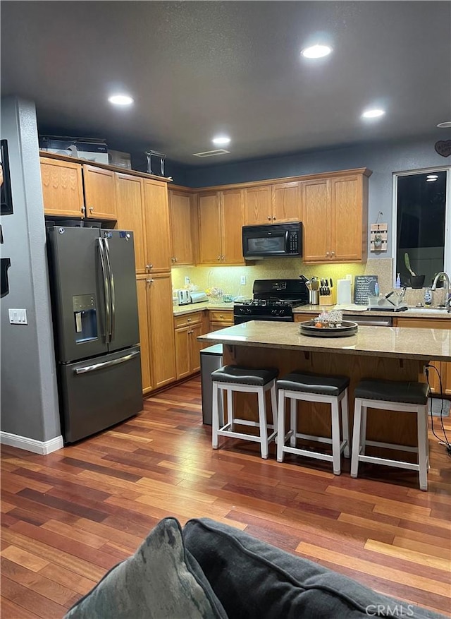 kitchen featuring tasteful backsplash, recessed lighting, a center island, dark wood finished floors, and black appliances