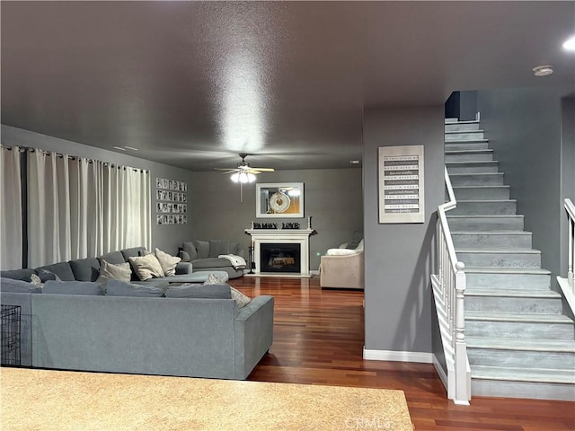 living area with stairs, a ceiling fan, a fireplace, baseboards, and dark wood-style flooring