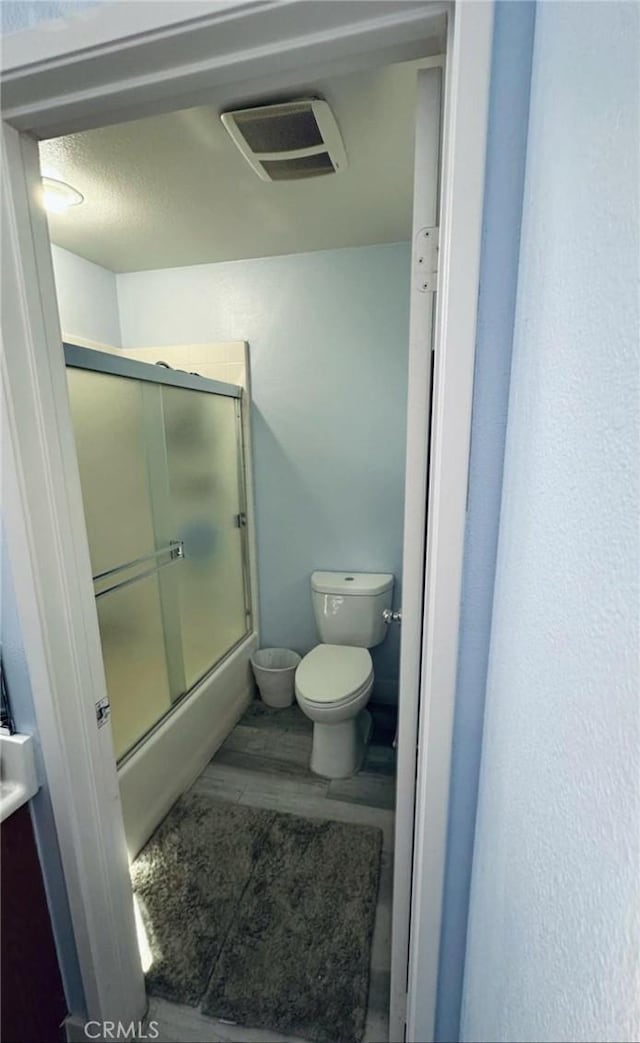 bathroom with visible vents, toilet, wood finished floors, and shower / bath combination with glass door