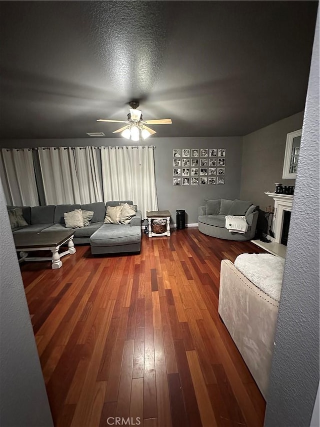 living room featuring a fireplace, a textured ceiling, ceiling fan, and wood-type flooring