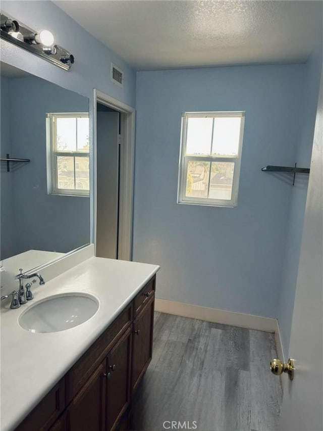 bathroom with vanity, wood finished floors, a textured ceiling, baseboards, and visible vents