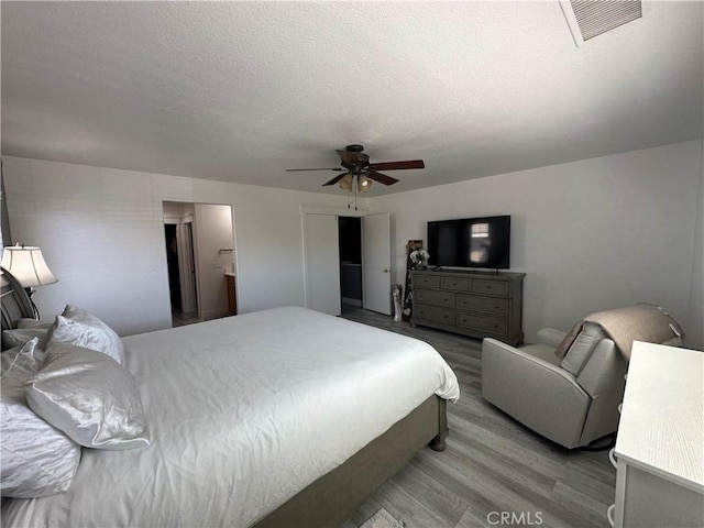 bedroom with a ceiling fan, wood finished floors, a textured ceiling, and visible vents