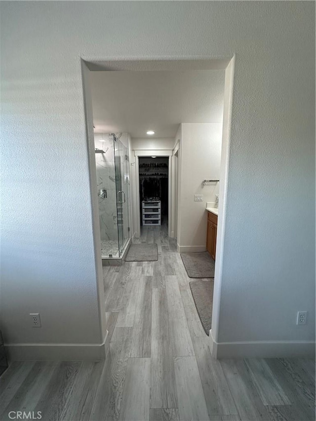 bathroom featuring vanity, a marble finish shower, a spacious closet, baseboards, and wood finished floors