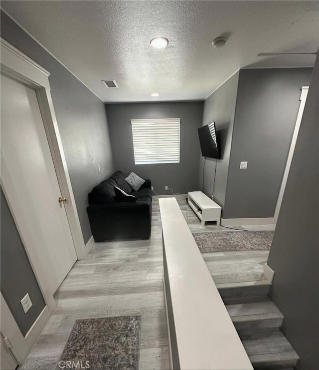 stairs with wood finished floors, a textured ceiling, baseboards, and visible vents