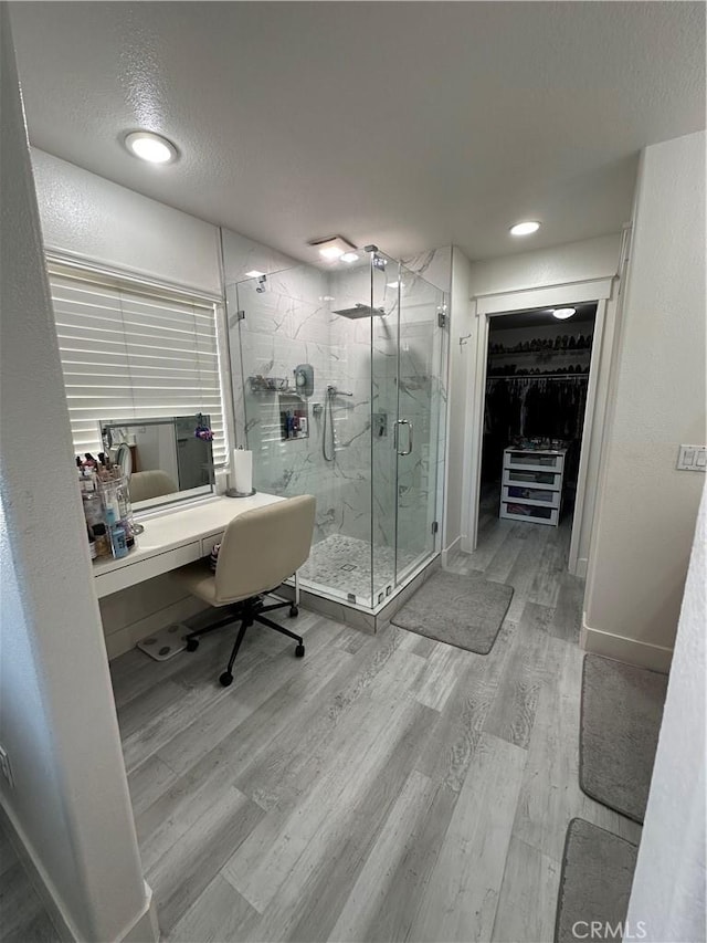 full bathroom featuring a marble finish shower, a spacious closet, baseboards, a textured ceiling, and wood finished floors