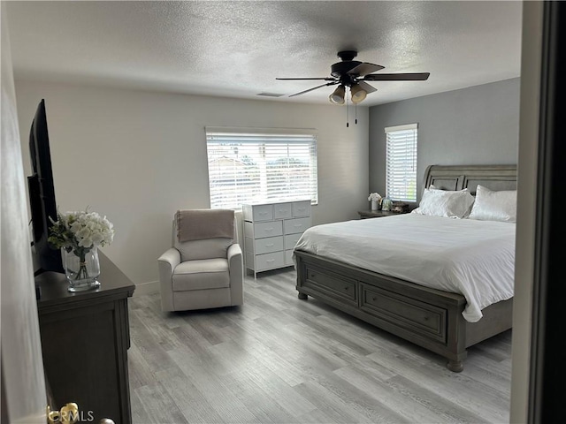 bedroom with a textured ceiling, visible vents, light wood-style floors, and ceiling fan