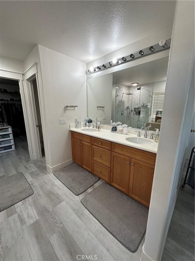 bathroom with a stall shower, a sink, wood finished floors, a textured ceiling, and double vanity