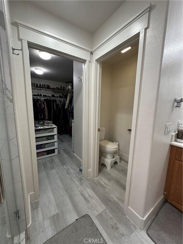 bathroom with vanity, a walk in closet, toilet, baseboards, and wood finished floors