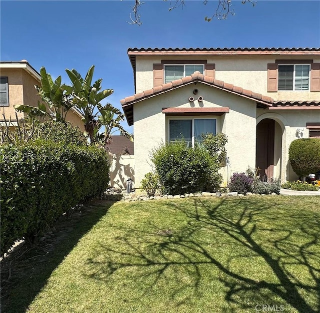 view of front of house featuring stucco siding, a tile roof, and a front yard