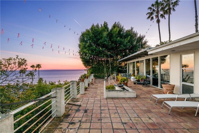 patio terrace at dusk featuring a water view