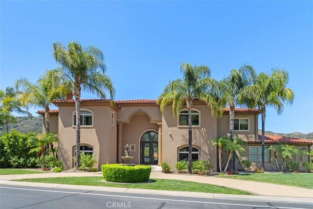 mediterranean / spanish home featuring french doors, a tiled roof, and stucco siding