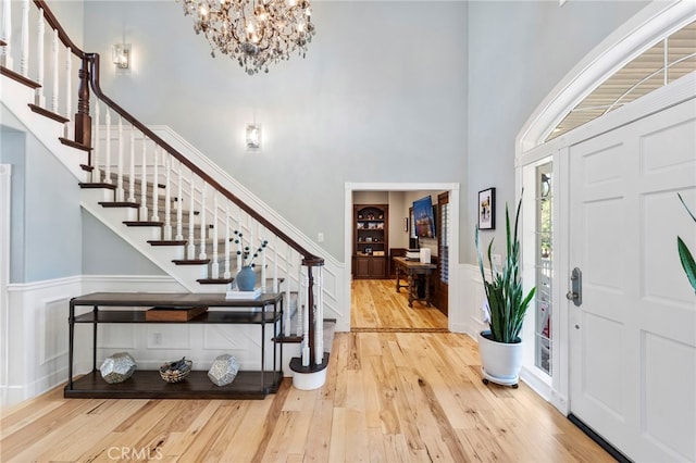 entryway with hardwood / wood-style floors, a high ceiling, a wainscoted wall, a chandelier, and stairs