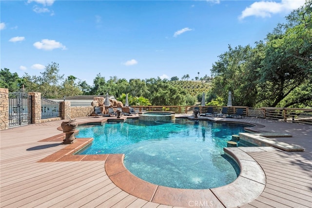 view of pool featuring fence, a wooden deck, and a pool with connected hot tub