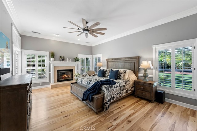 bedroom featuring a glass covered fireplace, light wood-type flooring, baseboards, and ornamental molding