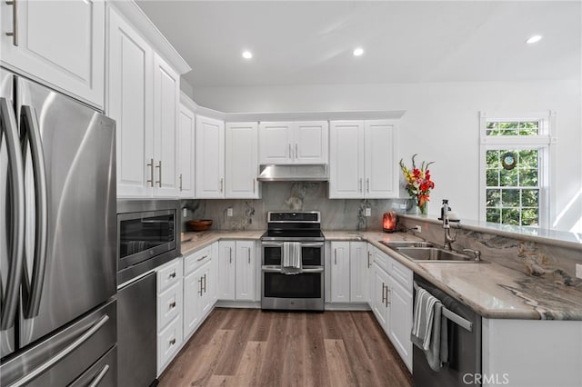 kitchen featuring white cabinets, dark wood-style floors, a sink, under cabinet range hood, and appliances with stainless steel finishes