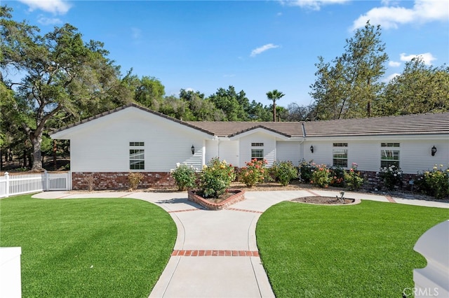 ranch-style home with brick siding, a tiled roof, a front yard, and fence