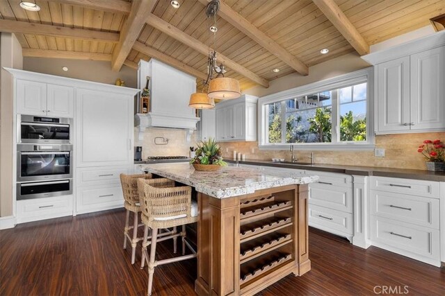 133 Upper Terrace Rd, Avalon, CA 90704 - kitchen featuring light stone counters, lofted ceiling with beams, custom exhaust hood, white cabinets, and a warming drawer