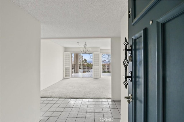entrance foyer with a textured ceiling, an inviting chandelier, light tile patterned floors, and light carpet