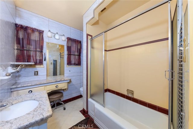 full bathroom featuring tile walls, combined bath / shower with glass door, toilet, tile patterned floors, and vanity