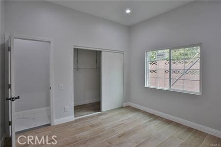 unfurnished bedroom featuring a closet, baseboards, light wood finished floors, and recessed lighting