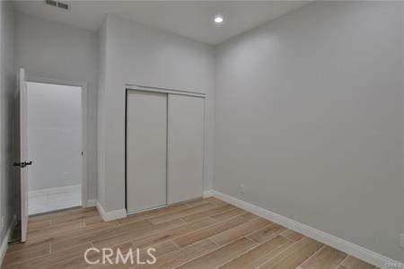 unfurnished bedroom with a closet, baseboards, light wood finished floors, and visible vents
