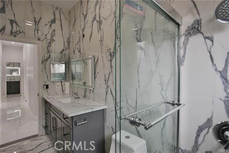 full bathroom featuring toilet, marble finish floor, vanity, and a marble finish shower