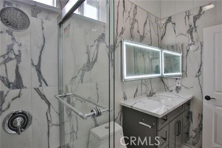 bathroom with vanity, a marble finish shower, and tile walls