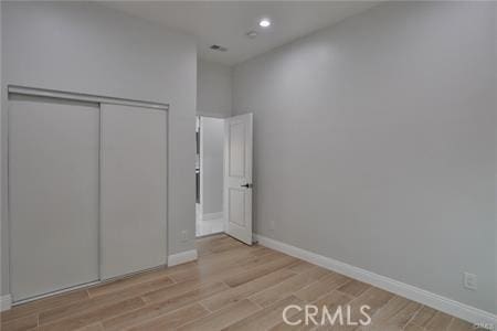 unfurnished bedroom with a closet, baseboards, light wood finished floors, and recessed lighting