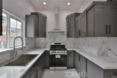 kitchen featuring stainless steel range with gas cooktop, wall chimney exhaust hood, a sink, gray cabinetry, and plenty of natural light