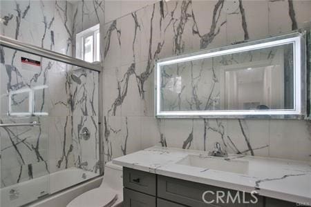 bathroom with toilet, vanity, and combined bath / shower with glass door