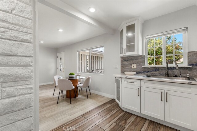 kitchen with wood finished floors, a sink, decorative backsplash, glass insert cabinets, and white cabinets