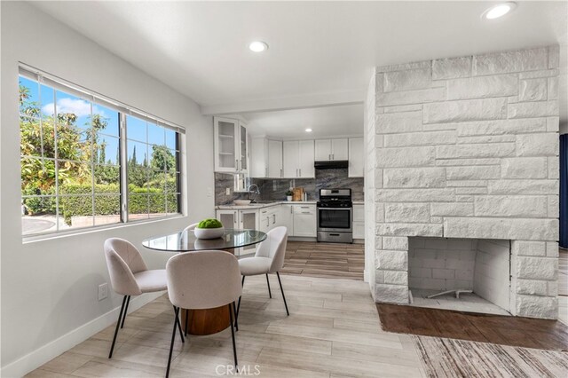 dining area with recessed lighting, a stone fireplace, light wood finished floors, and baseboards