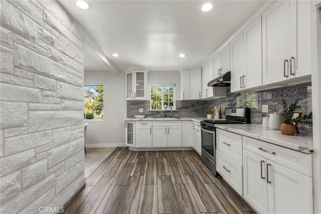 kitchen with white cabinets, a sink, tasteful backsplash, under cabinet range hood, and stainless steel gas range oven