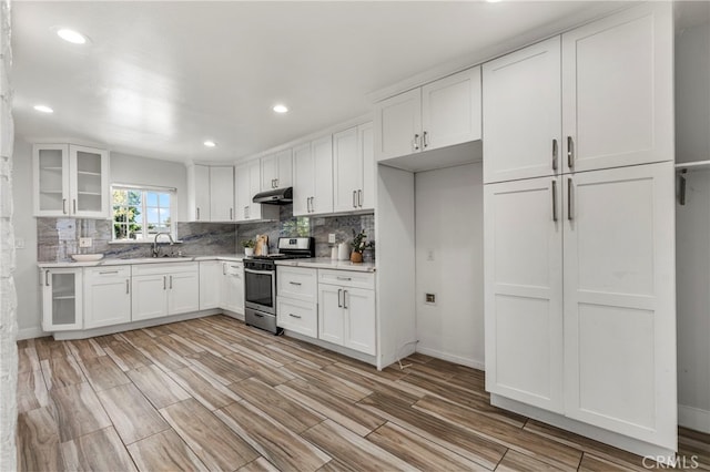 kitchen with under cabinet range hood, backsplash, light countertops, a sink, and stainless steel gas range