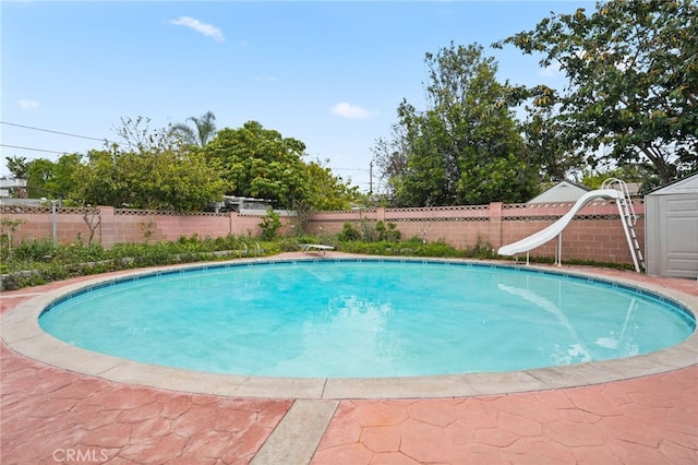 view of swimming pool featuring a storage shed, a fenced backyard, an outdoor structure, a fenced in pool, and a water slide