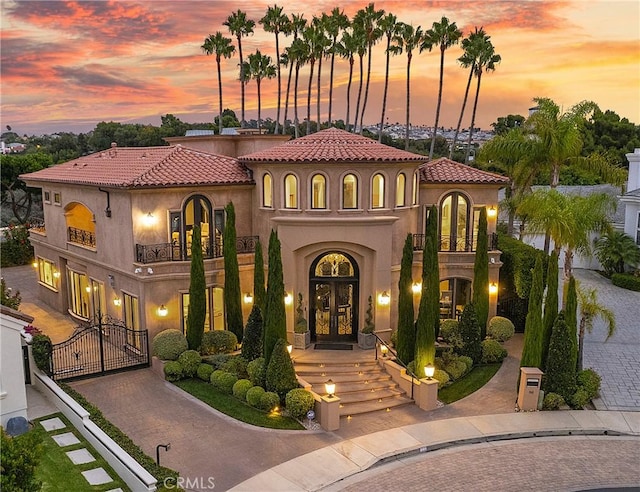 mediterranean / spanish home featuring a gate, french doors, curved driveway, stucco siding, and a balcony