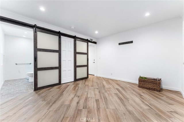 empty room with recessed lighting, baseboards, a barn door, and light wood-style flooring