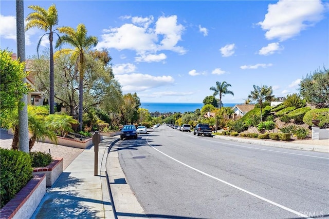 view of road featuring a water view, sidewalks, and curbs