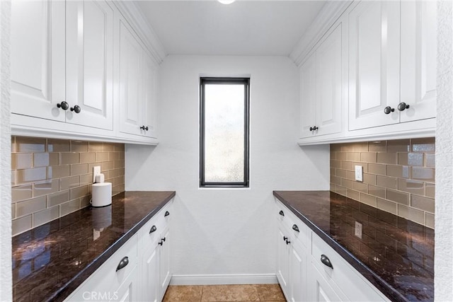 interior space featuring baseboards, decorative backsplash, dark stone countertops, and white cabinetry